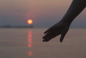 woman's hand silhouetted at waterside at sunset