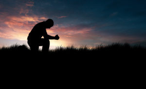 man praying with sunset in background