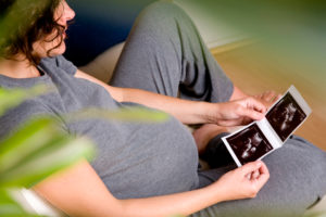 A pregnant woman sitting on a sofa looking at her unborn baby's ultrasound scan.